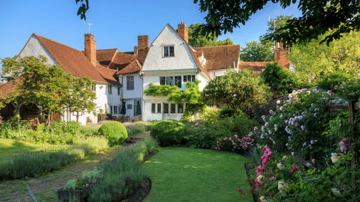 White house with red rooftiles, summer lawns and flowerbeds in front